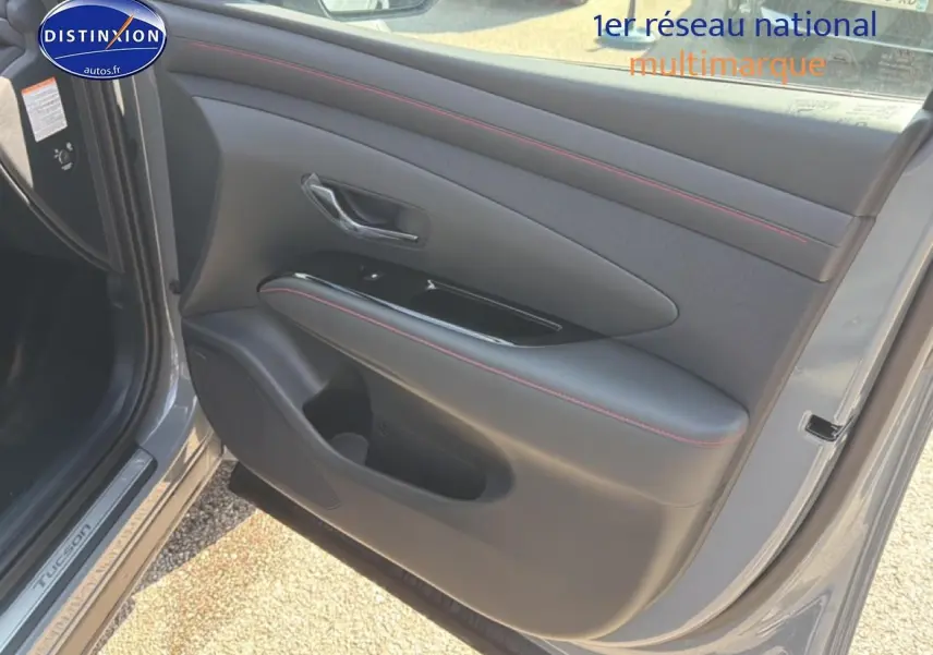 Vue rapprochée de la porte avant gauche gris shadow du Hyundai Tucson 2026 avec surpiqûres rouges et poignée chromée.