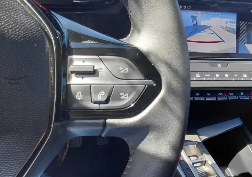 Gros plan sur le volant cuir noir et les commandes intégrées, avec l'écran tactile affichant la caméra de recul du Peugeot 308 gris.