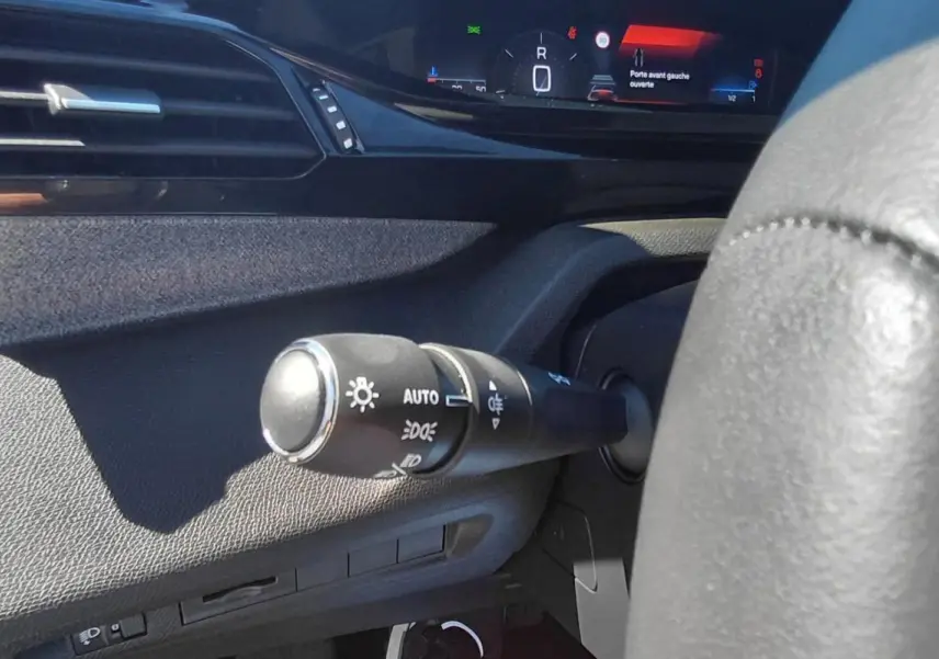 Gros plan sur la commande d’allumage automatique des feux côté gauche du tableau de bord d’une Peugeot 308 gris 2025.