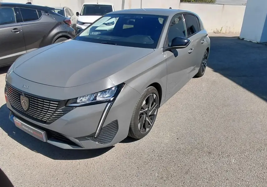 Peugeot 308 gris vue 3/4 avant droit, mettant en valeur sa calandre distinctive et ses phares LED fins.