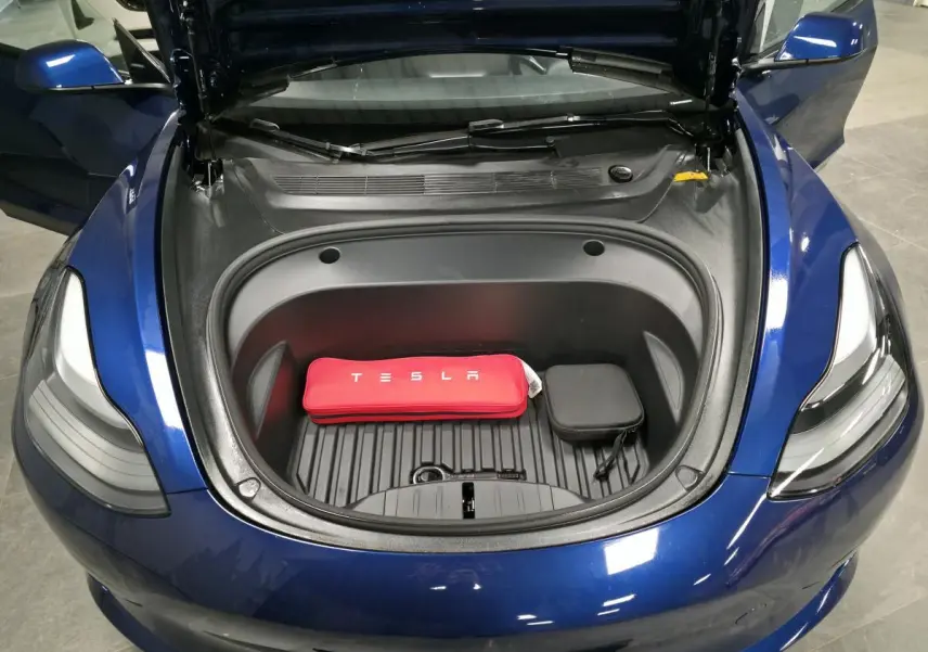 Vue plongeante sur le coffre avant ouvert d'une Tesla Model 3 RWD bleu foncé avec kit de recharge rouge visible.