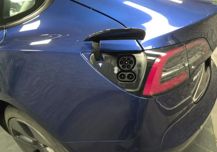 Prise de recharge ouverte sur l'aile arrière gauche d'une Tesla Model 3 RWD bleu foncé, avec feu arrière visible.