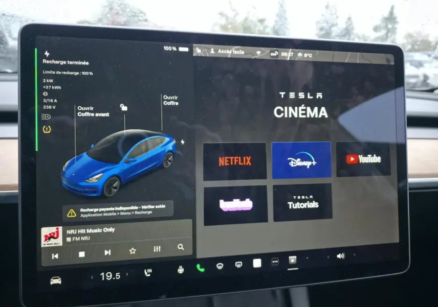 Écran tactile central affichant l'interface multimédia Tesla Cinema avec une illustration 3D d'une Model 3 bleu foncé.
