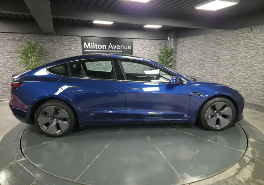 Vue latérale droite d'une Tesla Model 3 RWD 2021 bleu foncé avec jantes 18 pouces et poignées affleurantes.