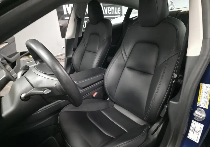Intérieur noir de la Tesla Model 3 RWD 2021, vue côté conducteur avec sièges en cuir et accoudoir central visible.