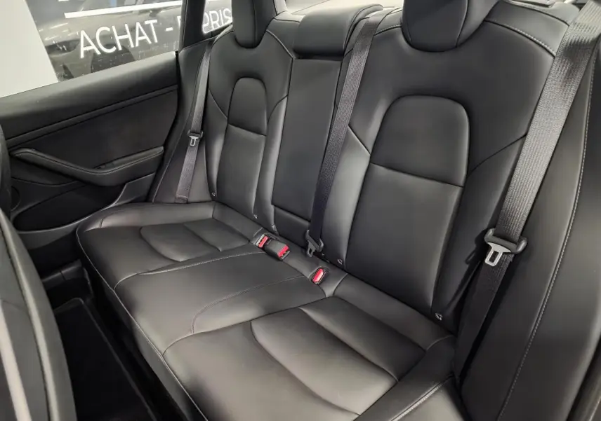 Vue latérale intérieure des sièges arrière noirs en cuir d'une Tesla Model 3 RWD 2021 avec ceintures grises.