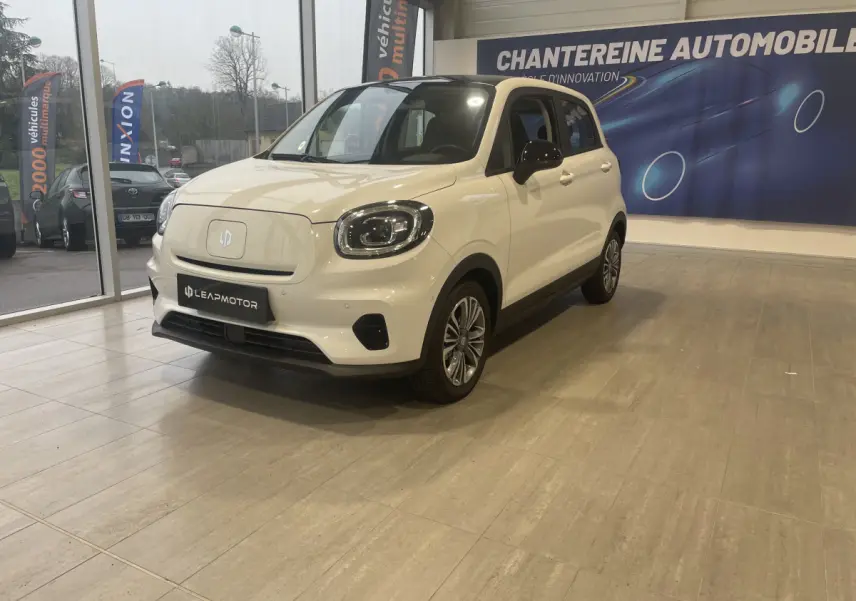 Vue 3/4 avant droite d'une LEAPMOTOR T03 Luxury blanche électrique en showroom avec phares LED et rétroviseurs noirs.