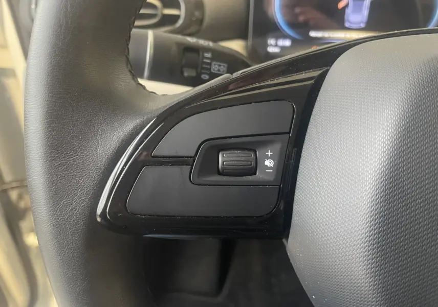 Gros plan sur la commande de volume du volant cuir noir du LEAPMOTOR T03 Luxury blanc, côté gauche.