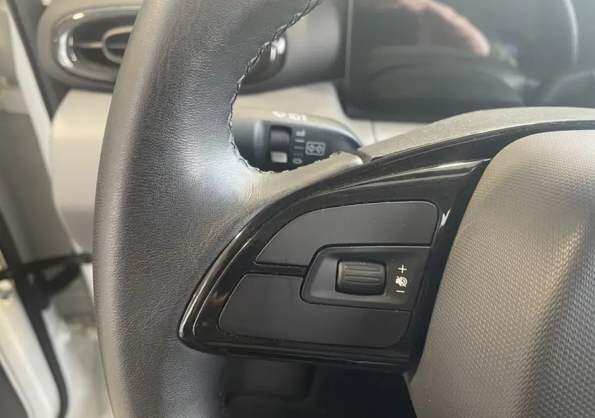 Gros plan sur le volant cuir multifonctions côté gauche du LEAPMOTOR T03 Luxury blanc, avec commandes intégrées.