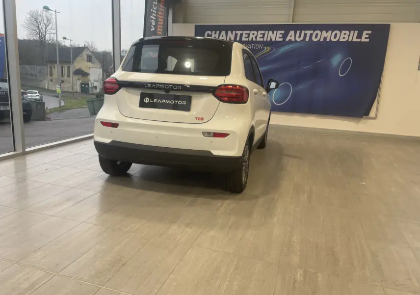 Vue 3/4 arrière d'une Leapmotor T03 Luxury blanche en showroom, avec feux arrière LED et toit noir contrastant.