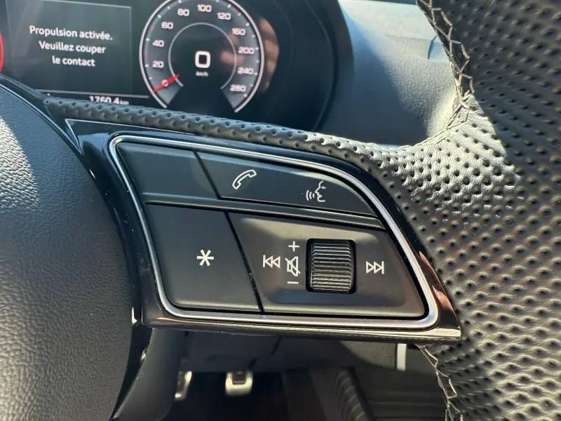 Gros plan sur les commandes au volant perforé de l'Audi Q2 35 TDI S line 2025, avec tableau de bord numérique en arrière-plan.
