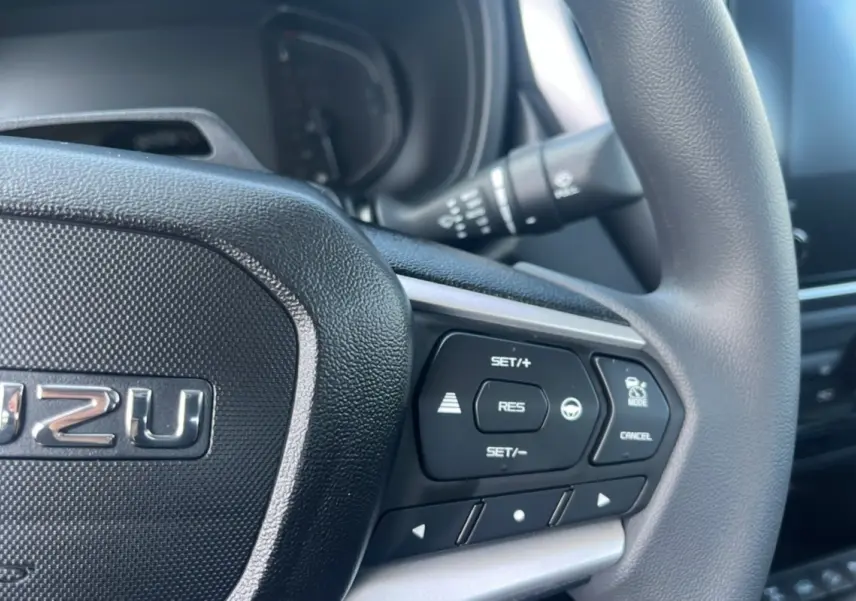 Gros plan sur le volant multifonctions noir de l'Isuzu D-MAX 2026 avec commandes de régulateur de vitesse visibles.