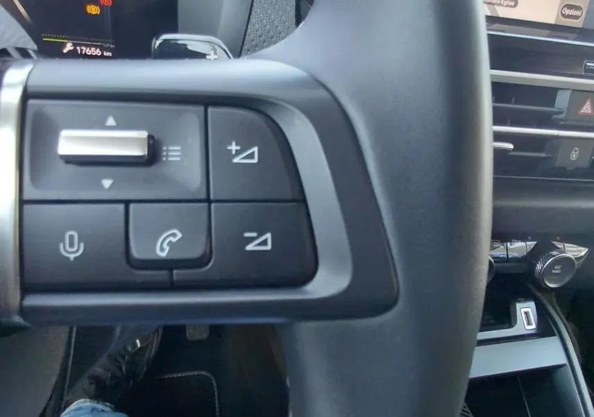 Gros plan sur les commandes du volant noir de la Citroën C4 X hybride 2025, avec tableau de bord et console en arrière-plan.