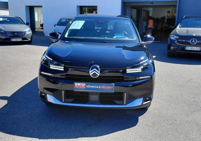 Vue avant d'une Citroën C4 X noire 2025 avec calandre distinctive et phares LED allumés.