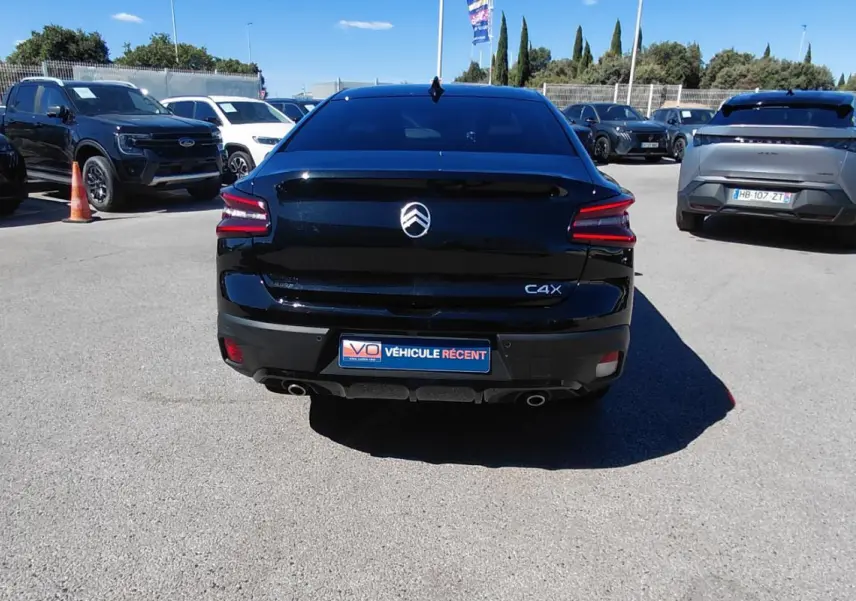 Vue arrière d'une Citroën C4 X noire 2025 avec feux LED et double sortie d'échappement visible sur parking.