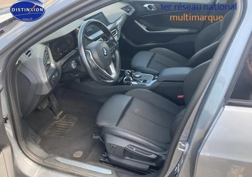 Intérieur côté conducteur d'une BMW Série 1 gris foncé 2023, volant sport cuir et sièges avant sport noirs.