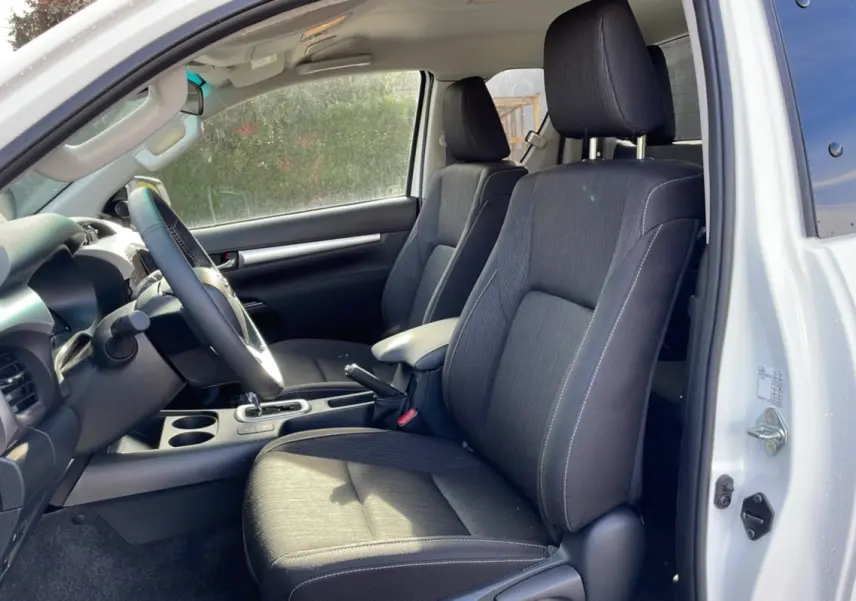 Intérieur du Toyota Hilux 4x4 blanc pur 2025, vue côté conducteur, sièges noirs et tableau de bord visible.