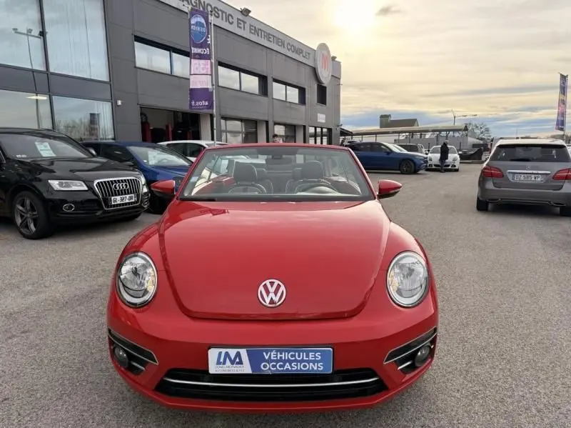 Volkswagen Coccinelle Cabriolet rouge vue de face, capote ouverte, sur parking devant un garage.