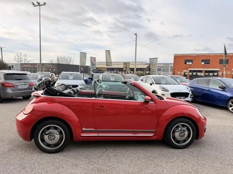 Vue de profil côté gauche d'une Volkswagen Coccinelle Cabriolet rouge 2016 avec capote ouverte et logo Denim sur la porte.