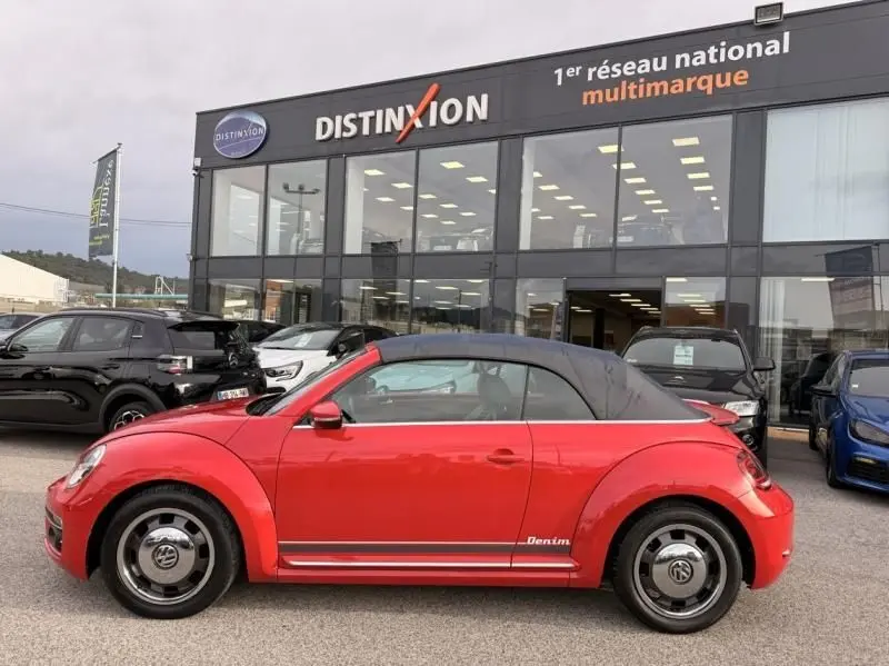 Vue latérale droite d'une Volkswagen Coccinelle Cabriolet rouge 2016 avec capote noire et bandeaux Denim sur le bas de caisse.