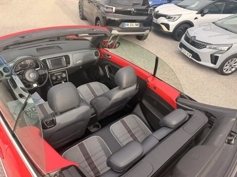 Vue intérieure en plongée de la Volkswagen Coccinelle Cabriolet rouge 2016, mettant en valeur ses sièges tissu gris avec surpiqûres rouges.