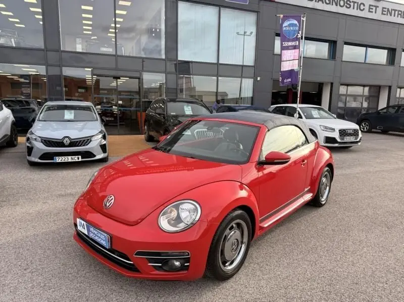 Volkswagen Coccinelle Cabriolet rouge vue 3/4 avant droit, capote noire fermée, stationnée devant un showroom.