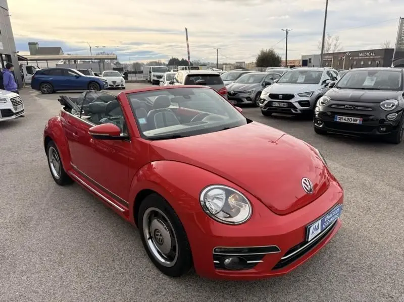 Volkswagen Coccinelle Cabriolet rouge vue en 3/4 avant, capote ouverte, jantes vintage et intérieur clair visible.