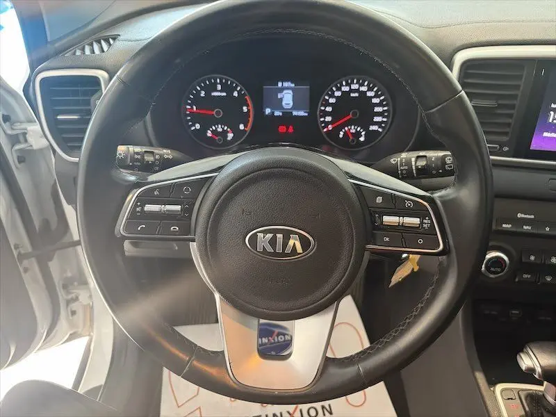 Vue centrée sur le volant noir du KIA Sportage blanc 2021, avec tableau de bord et commandes visibles.
