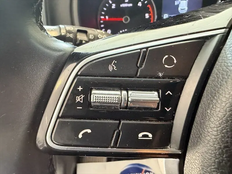 Gros plan sur les commandes noires du volant du KIA Sportage blanc, avec boutons de volume et téléphone visibles.