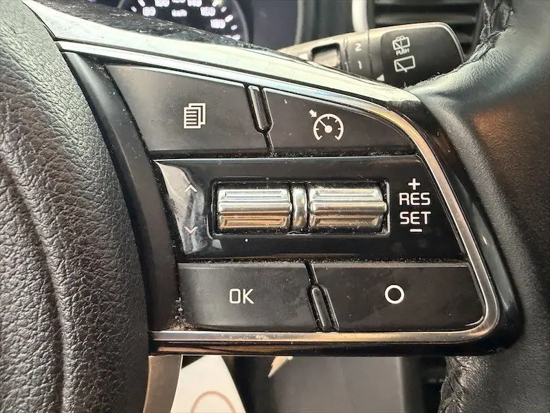 Gros plan sur les commandes de régulateur de vitesse au volant noir d’un KIA Sportage blanc 2021.
