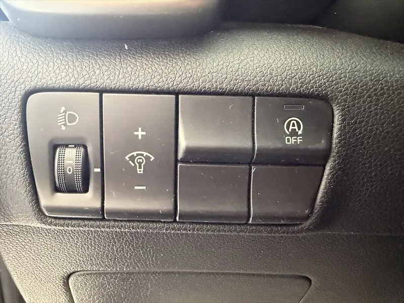 Gros plan sur les commandes de réglage des phares et désactivation du système start-stop dans un KIA Sportage blanc 2021.