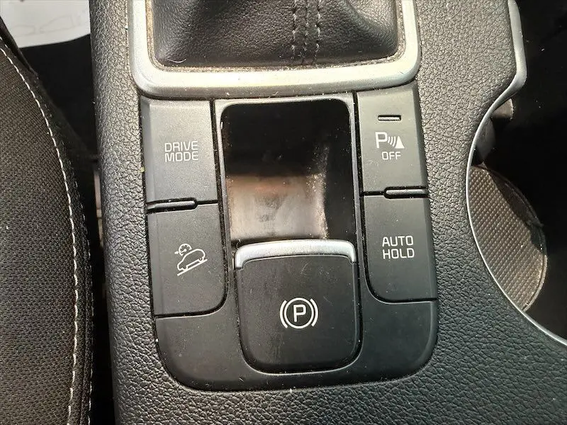 Vue rapprochée du panneau de commandes central du Kia Sportage blanc 2021, avec frein à main électronique et boutons Drive Mode et Auto Hold.