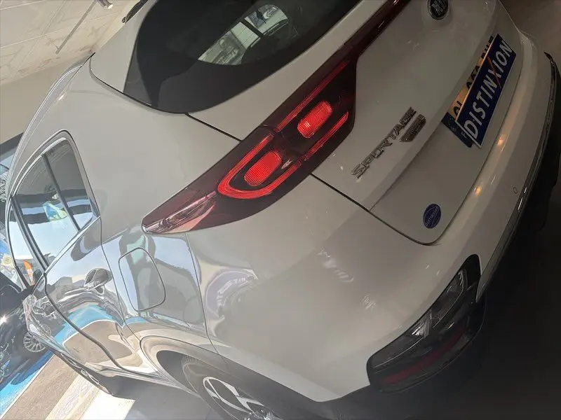 Vue 3/4 arrière droite d'un KIA Sportage blanc 2021 avec feux arrière allumés et logo distinctif sur hayon.