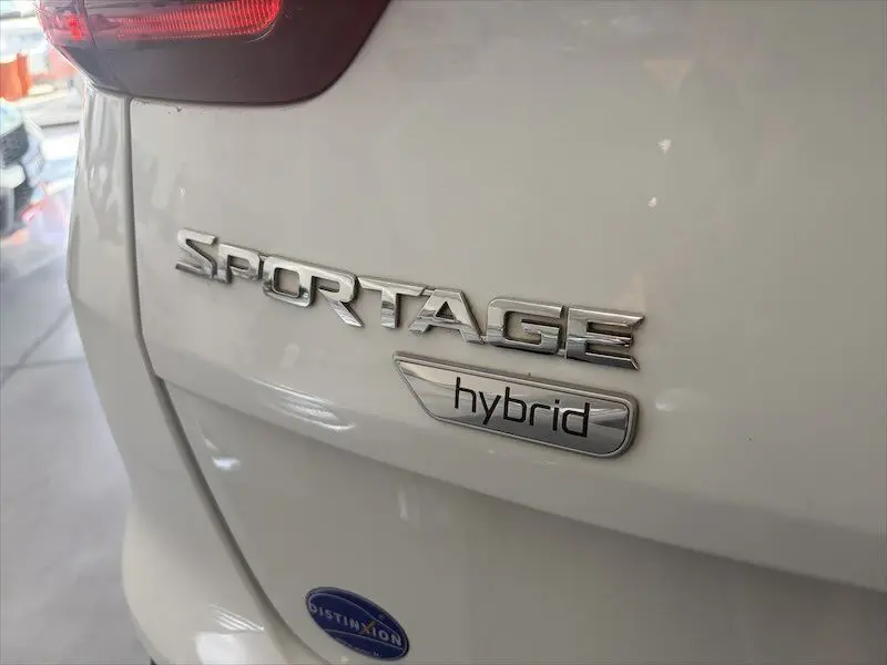 Gros plan sur l'arrière gauche d'un KIA Sportage blanc avec les badges "SPORTAGE" et "hybrid" visibles.
