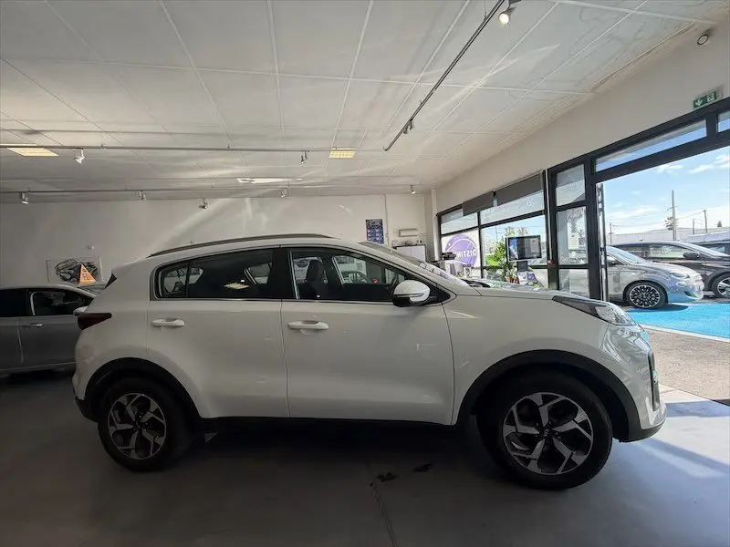 Vue de profil côté gauche d'un KIA Sportage blanc 2021 en intérieur, soulignant ses jantes alliage et lignes épurées.