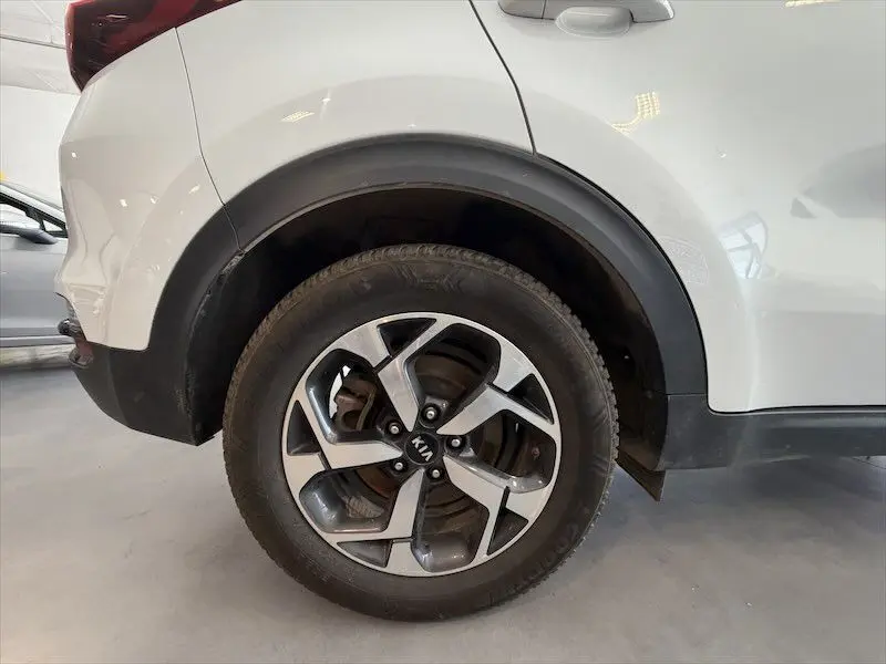 Gros plan sur la roue arrière droite d’un KIA Sportage blanc, mettant en valeur la jante alliage au design moderne.