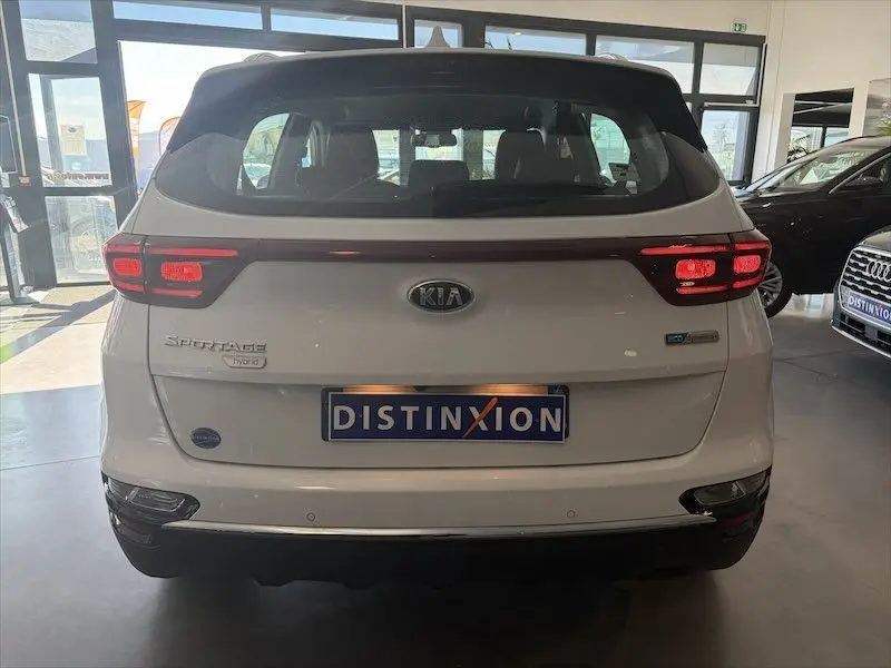 Vue arrière d’un KIA SPORTAGE blanc hybride, avec feux arrière allumés et plaque d’immatriculation Distinxion.