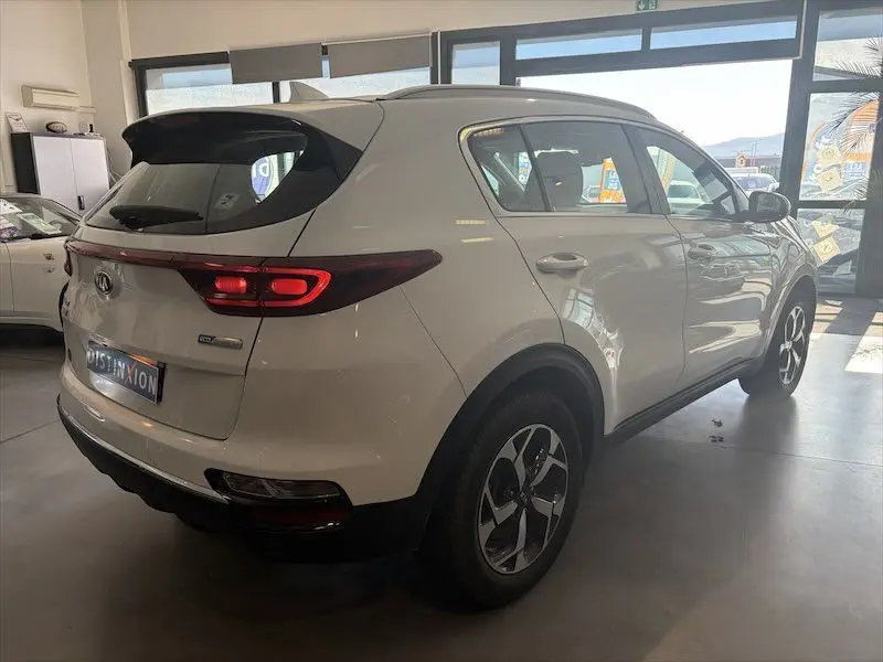 Vue 3/4 arrière droite d'un KIA Sportage blanc 2021 en intérieur, avec feux arrière allumés et jantes bi-ton.
