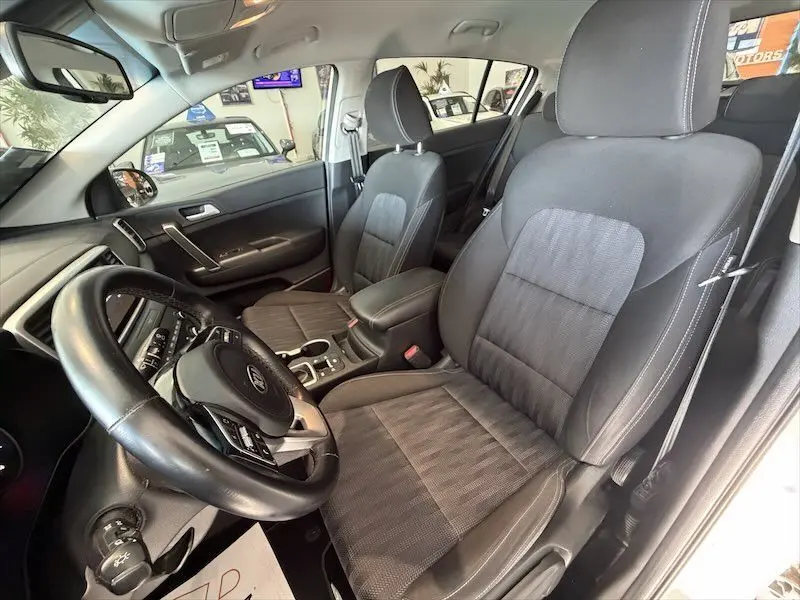 Vue intérieure côté conducteur du Kia Sportage blanc 2021, mettant en valeur les sièges noirs et le volant multifonction.