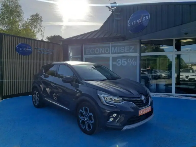 Renault Captur bleu marine fume en 3/4 avant droit, avec jantes alu et toit noir étoile, stationné devant un showroom.