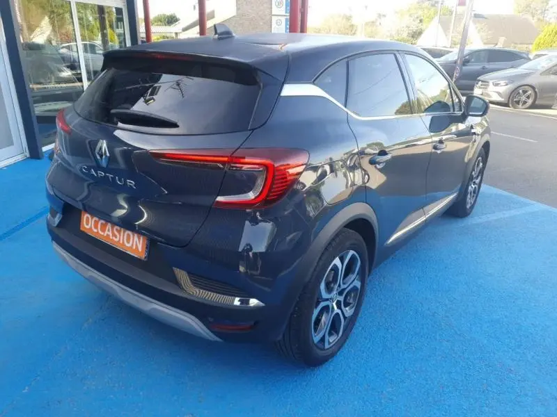 Vue 3/4 arrière droite d'un Renault Captur 2023 bleu marine fumé avec vitres teintées et jantes alu distinctives.
