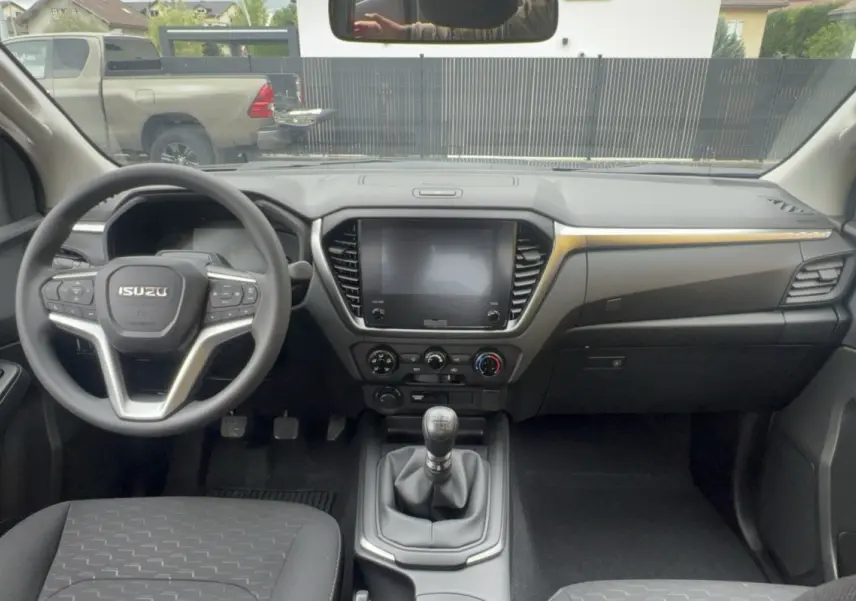 Vue intérieure avant de l'Isuzu D-MAX 2026, tableau de bord noir avec écran tactile et volant multifonctions.