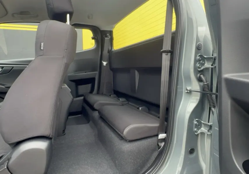 Vue intérieure côté arrière droit du pick-up Isuzu D-MAX 2.2 TD 164 Space Evolution avec banquette arrière rabattue et sellerie tissu noire.