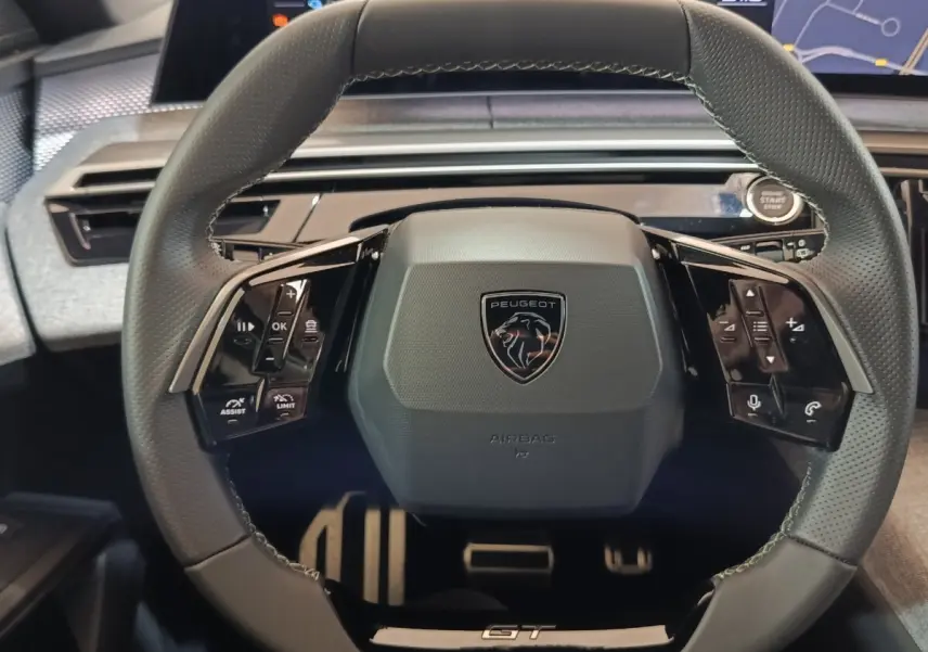 Vue rapprochée du volant cuir noir du Peugeot 5008 1.6 PHEV GT avec commandes multifonctions et logo central.