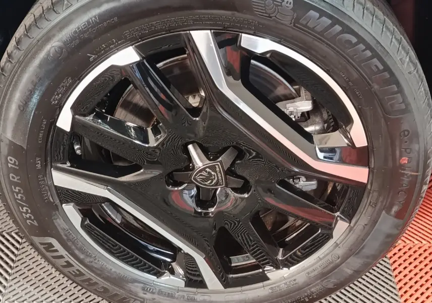 Gros plan sur la roue avant droite du Peugeot 5008 gris clair, jante alliage noire et argentée avec logo lion central.