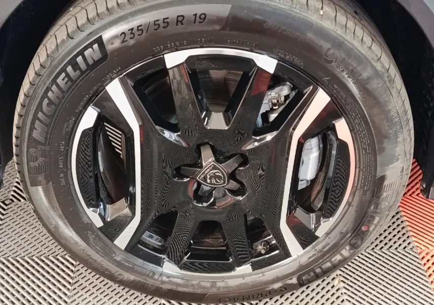 Gros plan sur la jante noire et argentée avec logo Peugeot, montée d’un pneu Michelin 235/55 R19, sur Peugeot 5008 gris clair.