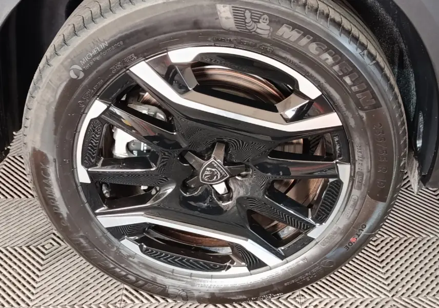 Gros plan sur la jante noire et argentée avec logo Peugeot, montée d’un pneu Michelin sur Peugeot 5008 gris clair.