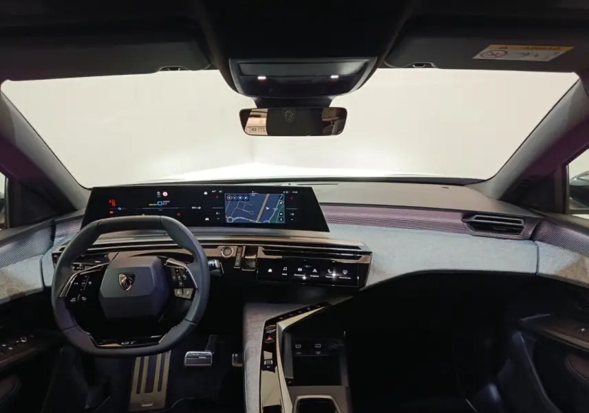 Vue intérieure avant du tableau de bord gris clair et noir du Peugeot 5008 1.6 PHEV 195 E-DCS7 GT avec écran tactile panoramique et volant multifonctions.