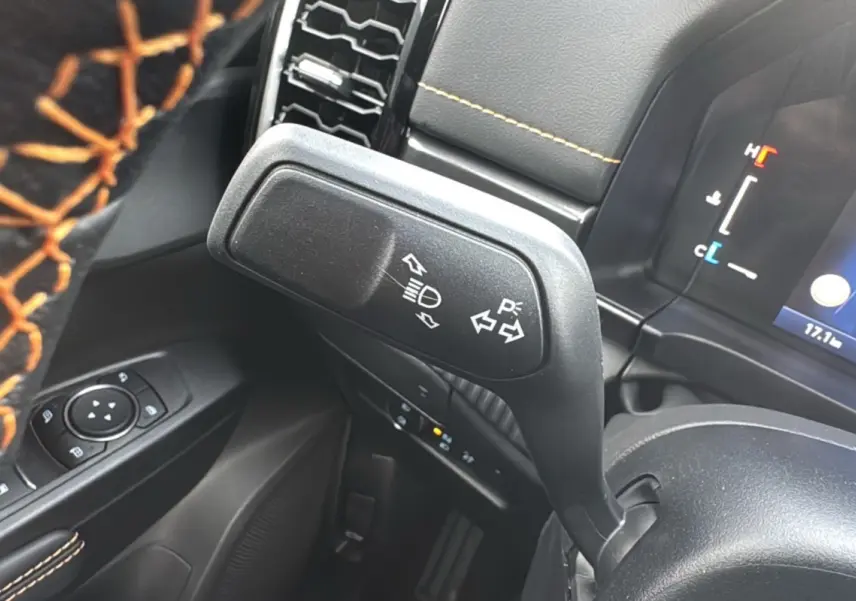 Gros plan sur la manette de clignotants et feux du Ford Ranger Wildtrak, intérieur noir avec surpiqûres orange.