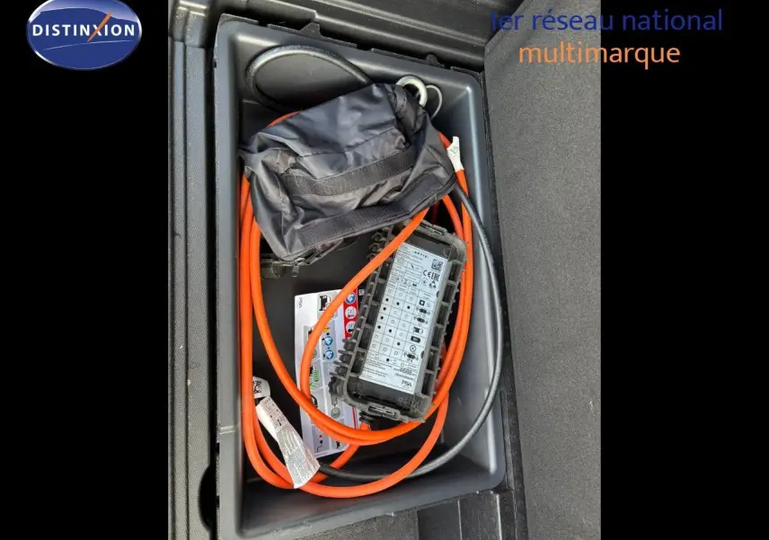 Coffre ouvert montrant le câble de recharge orange du Peugeot 3008 hybride gris platinium, vue plongeante sur le rangement.